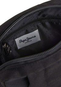 Juodos medžiagos maišelio vidus, demonstruojantis lygų pamušalą; turi užtrauktuką, baltą Pepe Jeans etiketę ir subtilius siuvimo akcentus.