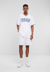 Hvit atletisk trøye med blå "FUBU"-tekst, korte ermer og svarte detaljer. Kombinert med matchende hvite shorts og hvite joggesko.