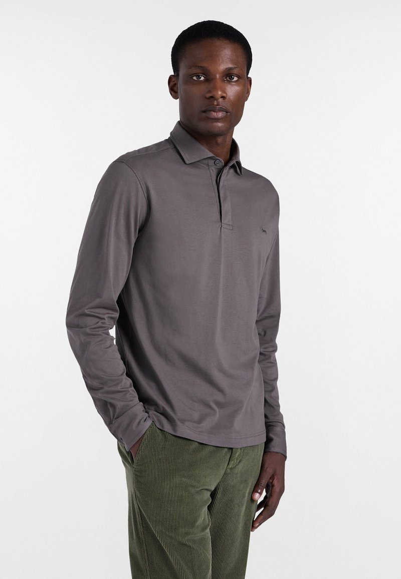 Granatowa bawełniana koszula polo z długim rękawem, z wywiniętym kołnierzykiem i małym haftowanym logo. Połączona z zielonymi spodniami z korduroju.