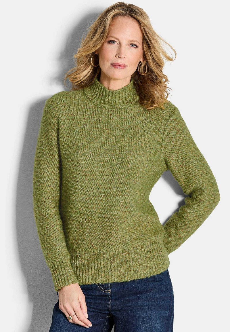 Grüner Strickpullover mit hohem Kragen, strukturiertem Stoff, gerippten Bündchen und Saum. Kombiniert mit dunkelblauen Jeans.