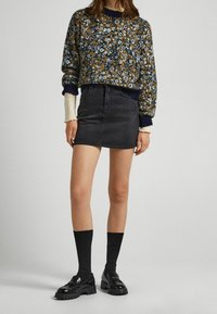 Pullover mit Blumenmuster in Marineblau und Senfgelb, mit gerippten Bündchen, kombiniert mit einem schwarzen Jeans-Minirock. Schwarze Loafers mit dicken Sohlen und knielange Socken.