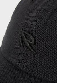 Black cap made of textured fabric featuring a black embroidered logo. Curved brim and stitched detailing visible on the surface.