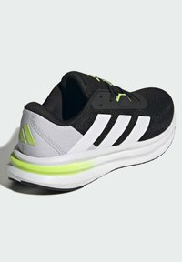 Czarny i szary but sportowy z białymi paskami, wykonany z teksturowanej siateczki, z wyściełaną podeszwą i neonowo zielonymi akcentami.