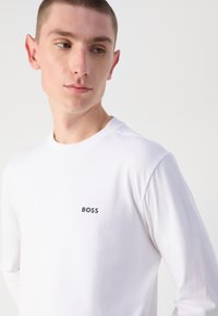 Langermet hvit T-skjorte i bomull med rund hals og en svart "BOSS"-logo på brystet, med en jevn tekstur og tettsittende design.