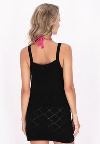 Abito nero senza maniche con motivo a diamante, busto aderente e design testurizzato. Rifinito con un fiocco rosa al collo.