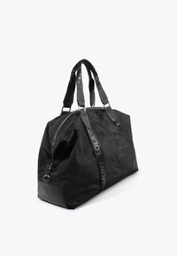 Svart duffelväska i texturerad nylon med matt finish, utrustad med dubbla handtag, dragkedjestängning och reflekterande varumärkesdetaljer.