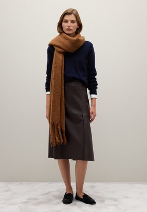 Sciarpa di lana marrone, maglione blu navy, gonna in pelle marrone e scarpe nere. Design strutturato, materiale testurizzato e palette di colori neutri.