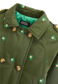  trench-coat vert brodé avec des motifs de fleurs jaunes, doté d'un col à revers, de boutons double boutonnage et d'une doublure vert vif.