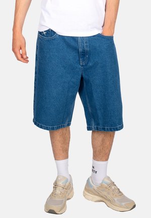 Denim shorts, blue, knee-length, featuring front pockets, a subtle logo, and stitched hems, paired with light sneakers and white socks.