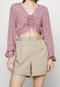 Top cropped con stampa floreale, maniche a sbuffo in viola, rosa e giallo. Pantaloni corti beige a vita alta con bottone decorativo in vita.