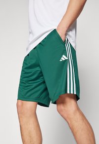 Vihreät urheilushortsit, jotka on valmistettu kevyestä kankaasta, valkoisilla sivuviivoilla ja Adidas-logo vasemmassa alakulmassa.