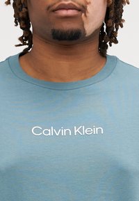 Μπλε βαμβακερό t-shirt με στρογγυλή ανοιχτή λαιμόκοψη; διαθέτει το λευκό λογότυπο "Calvin Klein" εκτυπωμένο κεντρικά στο στήθος; λεία υφή.