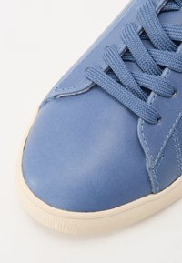 Light blue leather sneaker with textured surface, featuring flat laces, stitched accents, and a cream rubber sole.