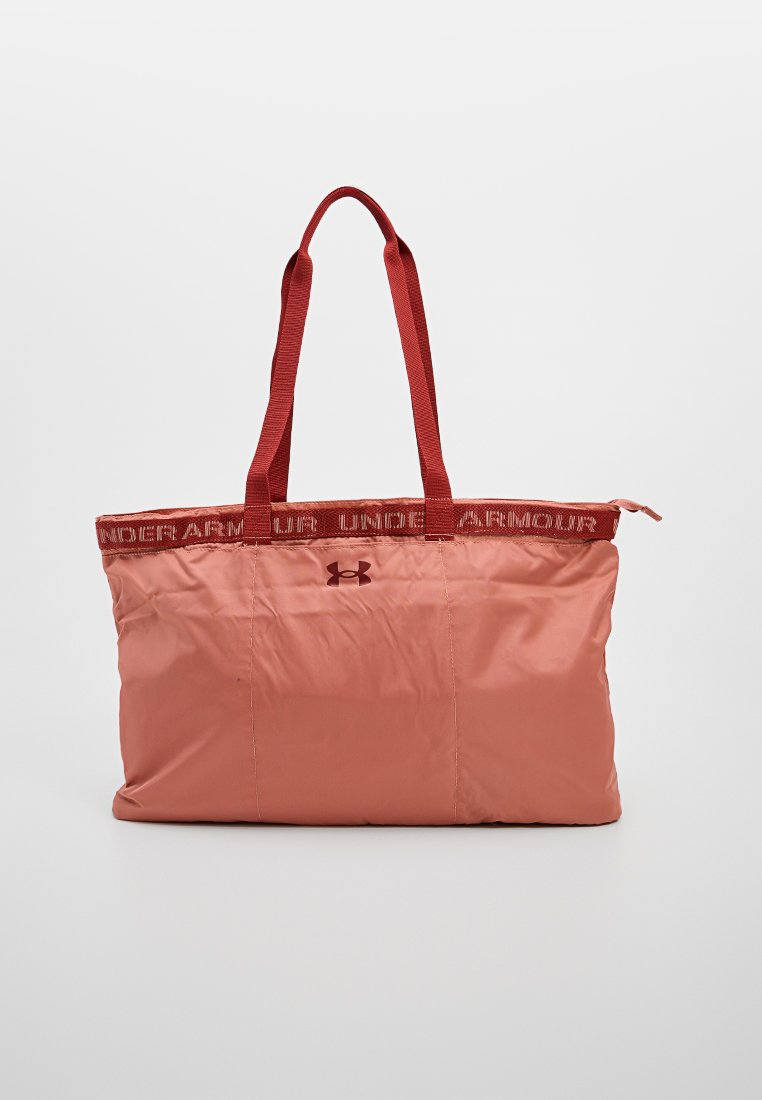 Bolso de lona de nylon rosa con asas de tela rojas. Presenta una parte superior elasticada y el logo de Under Armour en el centro. Textura suave y ligera.