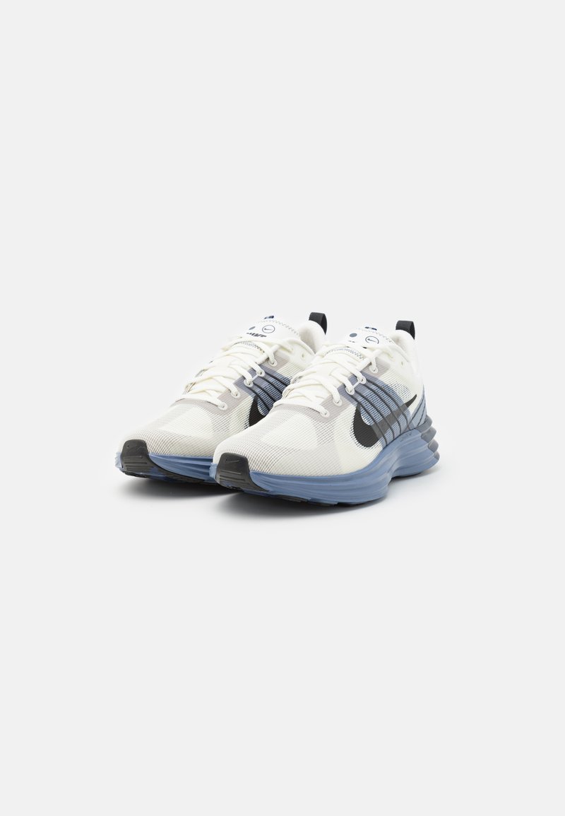 Zapatillas deportivas blancas con parte superior de malla, acentos en azul y negro, punta redondeada, sistema de cordones visible y suela texturizada.
