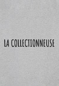 Tessuto grigio con testo ricamato in nero che legge "LA COLLECTIONNEUSE." Design semplice con una superficie leggermente strutturata.