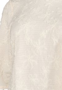 Blusa bianca testurizzata con un motivo floreale a strati, in tessuto morbido e dal taglio ampio con maniche a tre quarti.