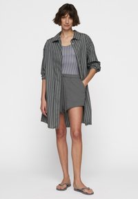 Camicia leggera a righe grigie, abbinata a un top in tinta unita grigio e a pantaloni corti. Sandali completano il look casual. Texture morbida in tutto il capo.