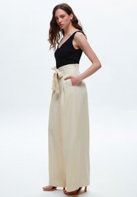 Zwarte geribbelde tanktop gecombineerd met hoge beige broek met een strikriem en zijzakken, van een soepele stof en met een brede pijp.