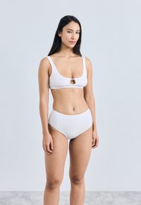 Λευκό ριμπ μαγιό μπικίνι που περιλαμβάνει τοπ βραλέτα με κυκλικό άνοιγμα και ψηλόμεσο σλιπ, φτιαγμένο από απαλό ύφασμα.