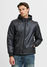 Schwarze gepolsterte Jacke mit Reißverschluss, Kapuze und Kordelzug. Verfügt über elastische Bündchen und seitliche Taschen sowie eine glatte, glänzende Textur.