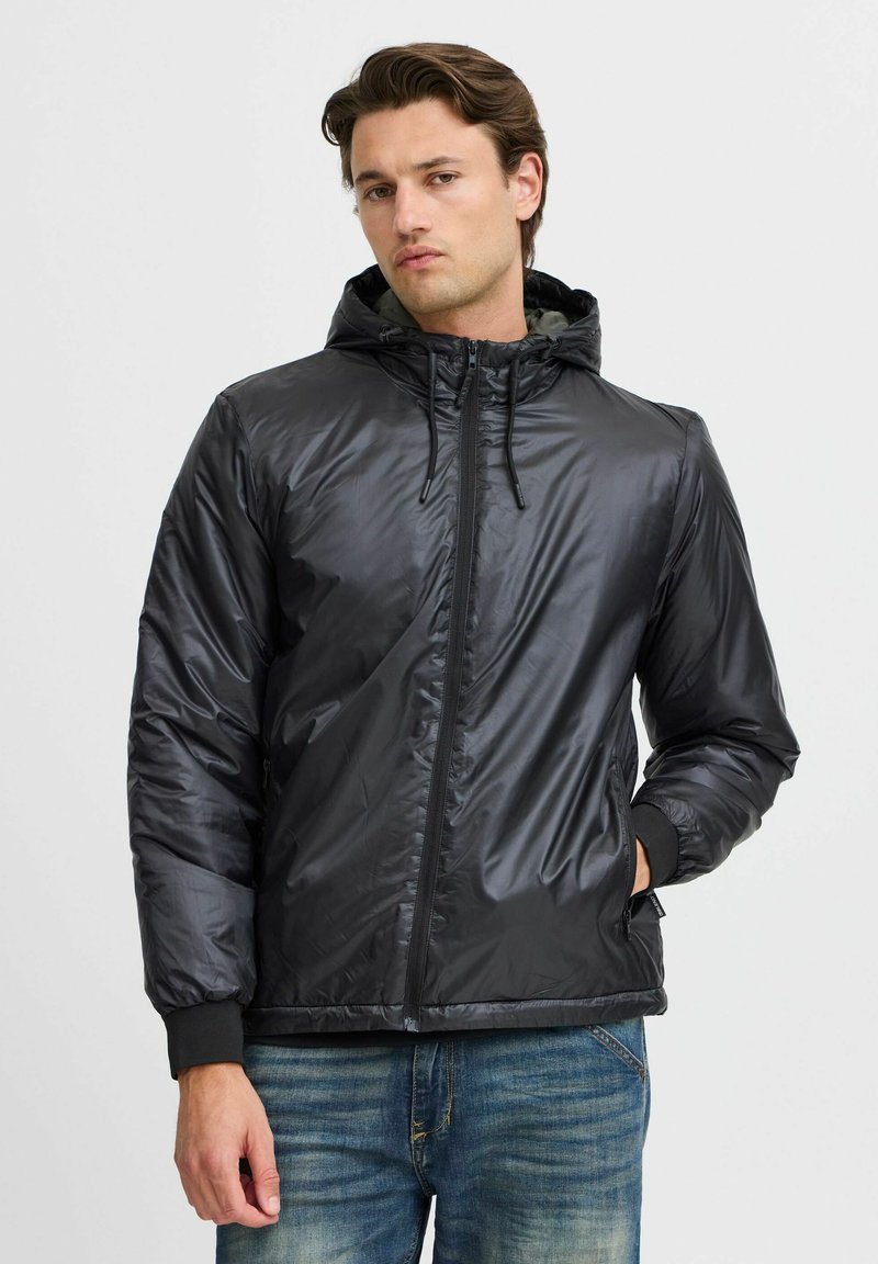 Schwarze gepolsterte Jacke mit Reißverschluss, Kapuze und Kordelzug. Verfügt über elastische Bündchen und seitliche Taschen sowie eine glatte, glänzende Textur.