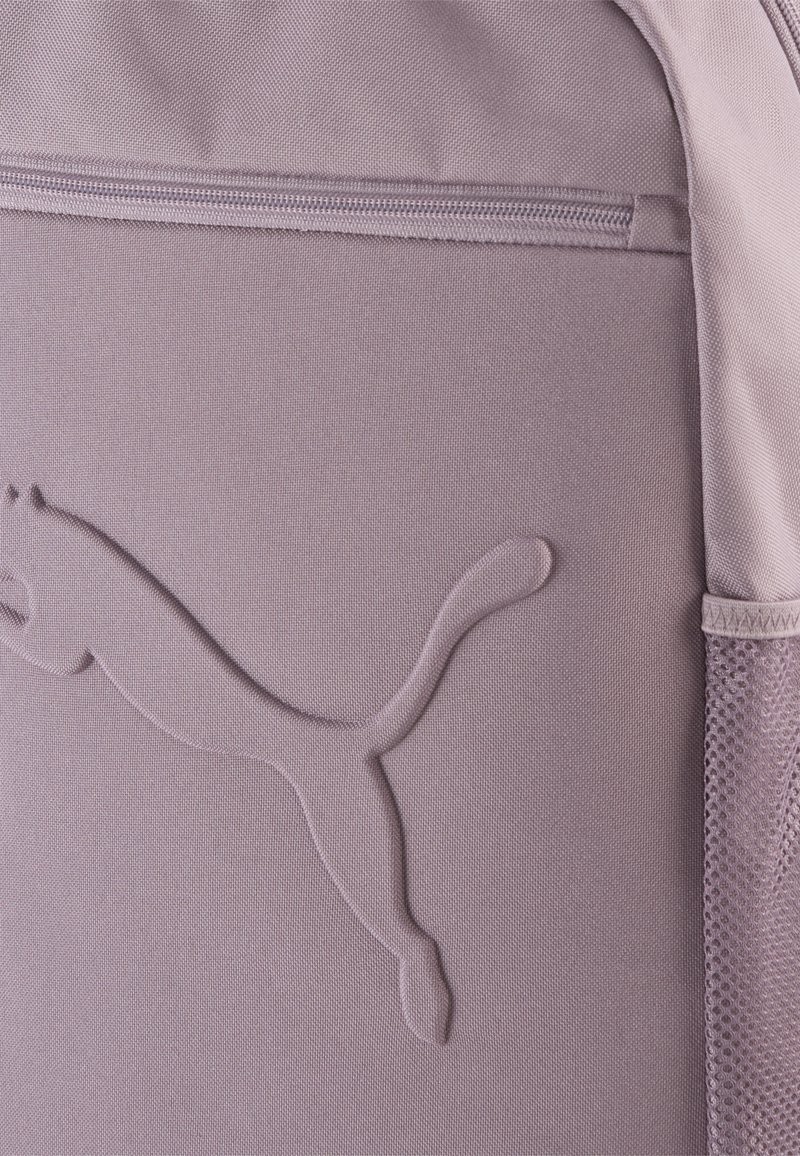 Sac à dos en tissu violet avec un logo Puma texturé, fermeture éclair et poche latérale en mesh pour un rangement supplémentaire.
