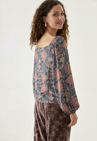 Blusa de estampado floral en tejido suave con mangas abullonadas, escote cuadrado y tonos coloridos de azul, rosa y verde. Realzada por drapeados.