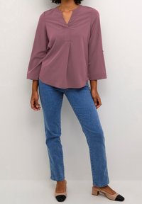 Blusa mauve con scollatura a V e maniche a tre quarti, abbinata a jeans in denim azzurro chiaro e scarpe con tacco a blocco beige con punte nere.