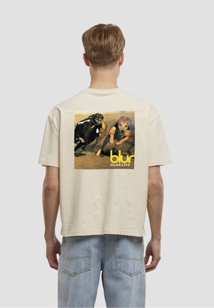 Világos bézs pamut póló, hátulján két versenyző kutyát ábrázoló grafikával. A mintán sárga színnel a „blur PARKLIFE” felirat szerepel.