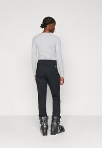 Μαύρο σκι παντελόνι με ομαλή υφή, σε εφαρμοστή γραμμή που στενεύει ελαφρώς προς τους αστραγάλους. Συνδυάζεται με μαύρες μπότες σκι.