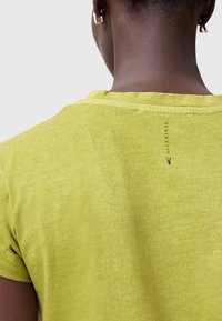 Limonkowa koszulka z krótkim rękawem, okrągłym dekoltem i widocznymi szwami. Mały detal z logo w okolicy karku z tyłu. Miękka tekstura.