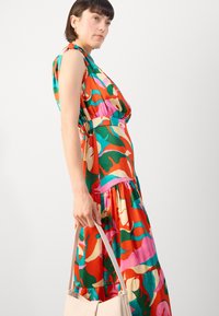 Robe maxi colorée et imprimée présentant des rouges, verts, roses et jaunes éclatants. Fabriquée en tissu léger avec une taille légèrement froncée et une jupe à volants.