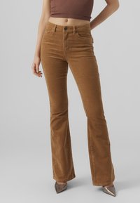Brown corduroy flared pants with a high waist, featuring front pockets and a textured surface. Paired with pointed metallic heels.