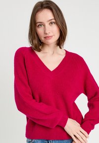Suéter vibrante de fucsia, textura de punto, diseño de cuello en V, mangas largas, detalles acanalados en los puños y el dobladillo, ajuste relajado.
