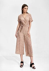 Różowy kombinezon wykonany z lekkiej tkaniny, z krótkimi rękawami, z wiązaniem w talii, szerokimi nogawkami i subtelnym wzorem ptaków. Noszony z czarnymi szpilkami.