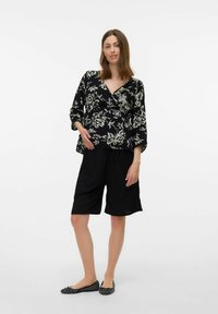 Top de flores negras con mangas tres cuartos, combinado con pantalones cortos negros holgados. La modelo lleva zapatos planos negros con estampado. Tela suave y ligera.