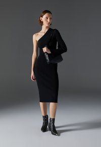 Vestido de punto acanalado negro con una manga larga, hasta la rodilla. Combinado con un bolso negro y botas de tobillo negras con ojales plateados y puntera afilada.