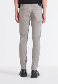 Jeans de denim gris claro con corte slim, que cuentan con dos bolsillos traseros y una textura suave. Llevados con botines negros.