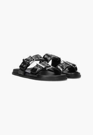 Black patent leather sandals with two wide straps featuring silver hardware and decorative eyelets. Flat sole and sleek design.