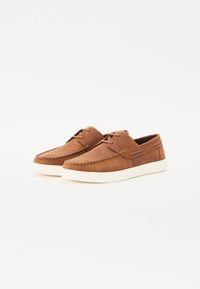 Hnedé kožené topánky s hladkým povrchom, okrúlym špičkou a bielou gumovou podrážkou. Obsahujú šikovne vykonané švy a dizajn so šnurovaním.