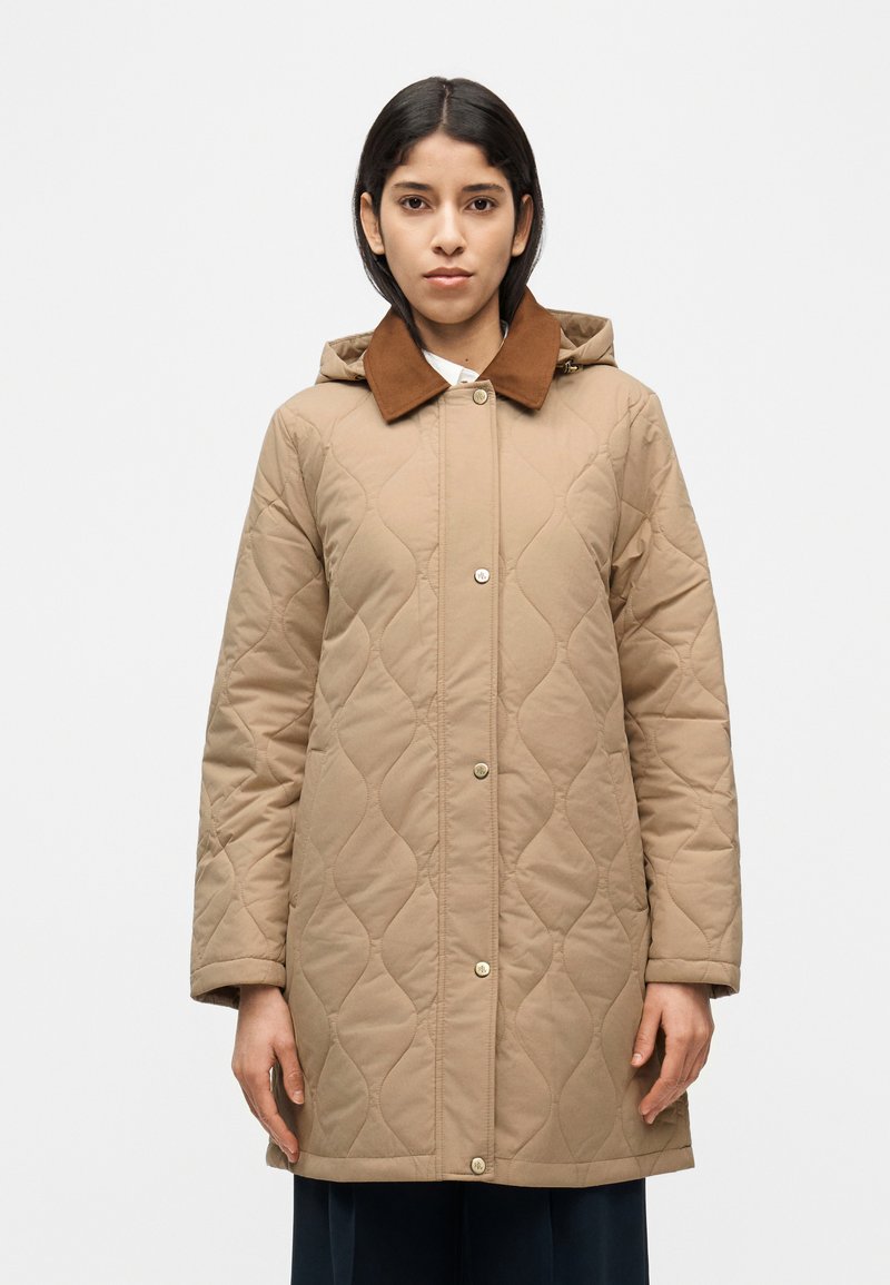 Μπεζ καπιτονέ παλτό με καφέ γιακά, διαθέτει κουκούλα, κουμπιά με τρουκ και υφή επιφάνειας. Μακριά μανίκια και ξεκάθαρη ίσια γραμμή.