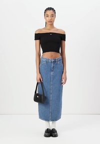 Top nero scollato, gonna midi in denim blu, calzini bianchi, mocassini neri e una piccola borsa nera, indossati su uno sfondo semplice.