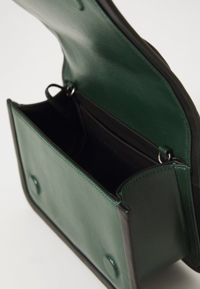 Petit sac à main en cuir vert foncé avec rabat ouvert, montrant un intérieur lisse et des attaches en anneau métallique sur un fond blanc.
