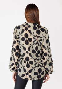 Blusa fluida e semi-trasparente con un motivo floreale nero su uno sfondo verde chiaro. Maniche lunghe con polsini elasticizzati e orlo curvo.