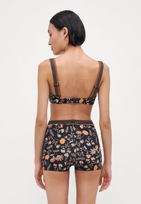 Juodasis bikinio viršus ir apačia su gėlių raštu ir oranžiniais akcentais. Dizainas pasižymi plačiomis petnešomis, tekstūruotais juostomis ir prigludusia forma.