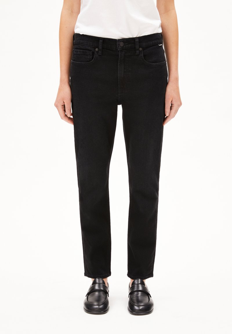 Svarta denimjeans med rak skärning, med fem fickor och knappstängning. Bärs med svarta loafers, uppvisade mot en vit bakgrund.