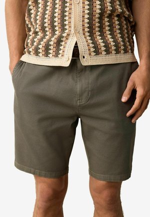 Pantaloni scurți dintr-un amestec de bumbac de culoare verde măsliniu, cu o croială clasică, dotati cu buzunare laterale și o textură netedă, asortați cu o cămașă cu model, cu nasturi.