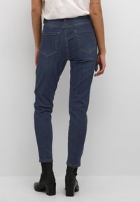 Mörkblå denim skinny jeans med medelhög midja, med två bakfickor och synliga sömnadsdetaljer. Bärs med ankelstövlar.