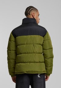 Puffjakke med sort overdel og olivengrøn underdel, featuring puffede sektioner, høj krave og ribbede manchetter. Blød tekstur, afslappet design.
